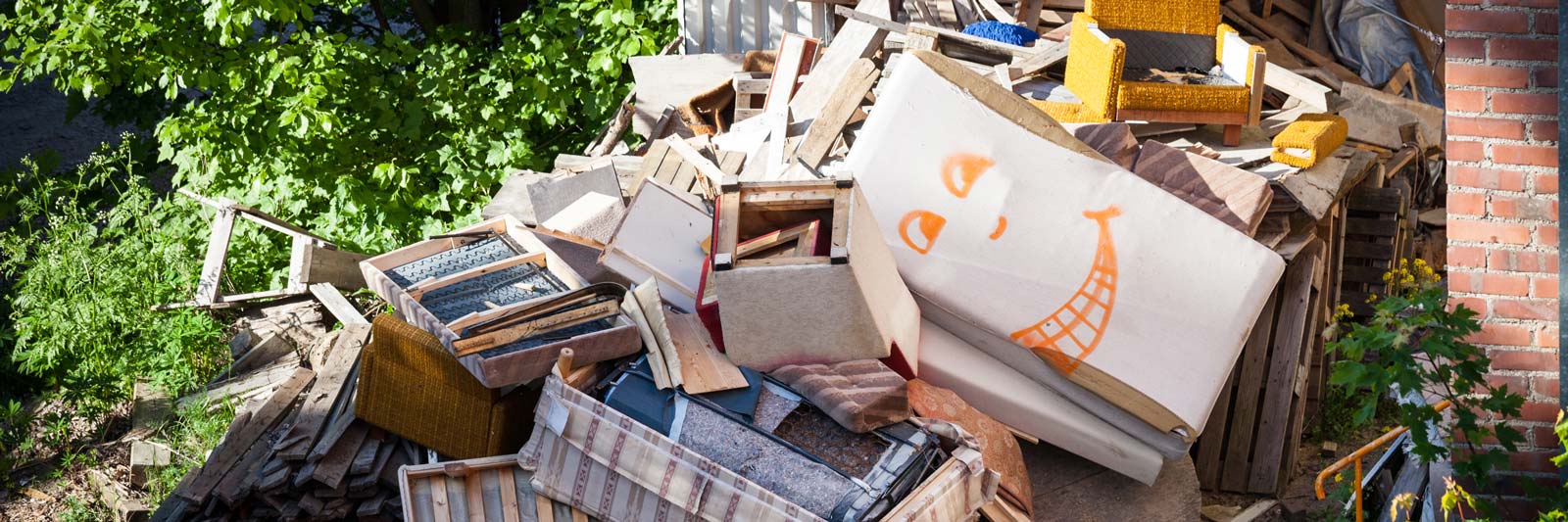Cumulo di mobili vecchi ammassati all'aperto: armadio, poltrona e legname pronti per lo smaltimento